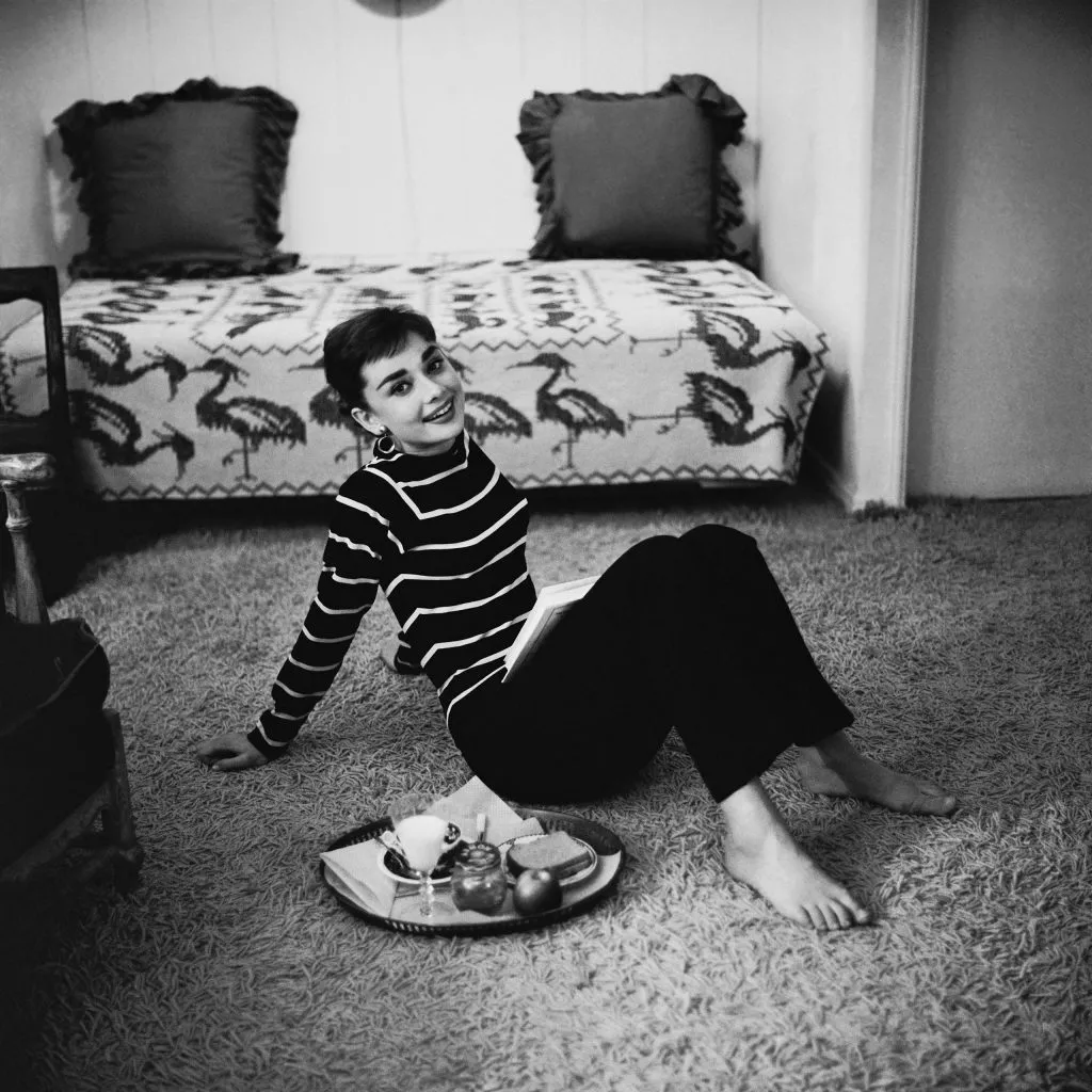 Audrey Hepburn sitting on the floor while eating and reading, reflecting her ballet-trained posture and calm routine