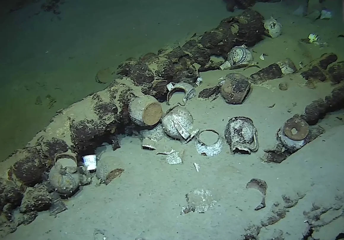 Underwater view of ceramic vessels and wreck fragments resting on the seafloor at the Camarat 4 shipwreck site.