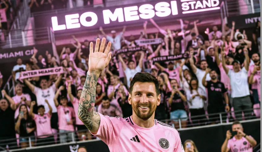 An Inter Miami player in a pink kit waves in front of cheering fans beneath the Leo Messi Stand at Nu Stadium.